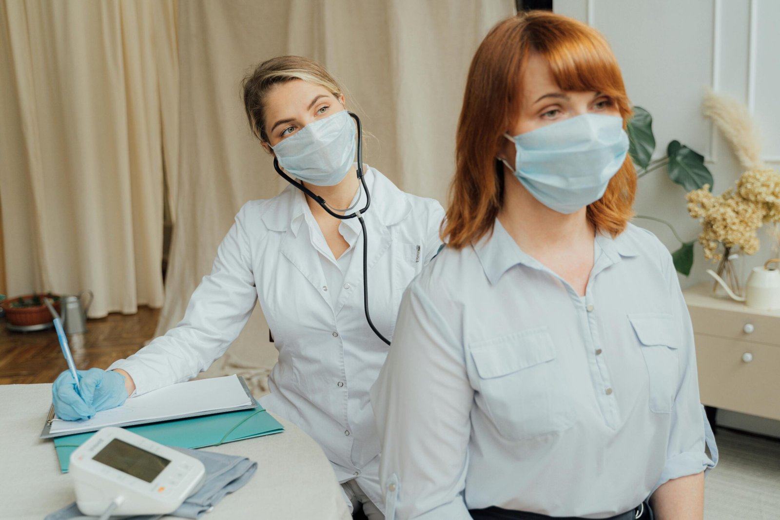 A healthcare worker in a mask conducts a medical examination on a masked patient.